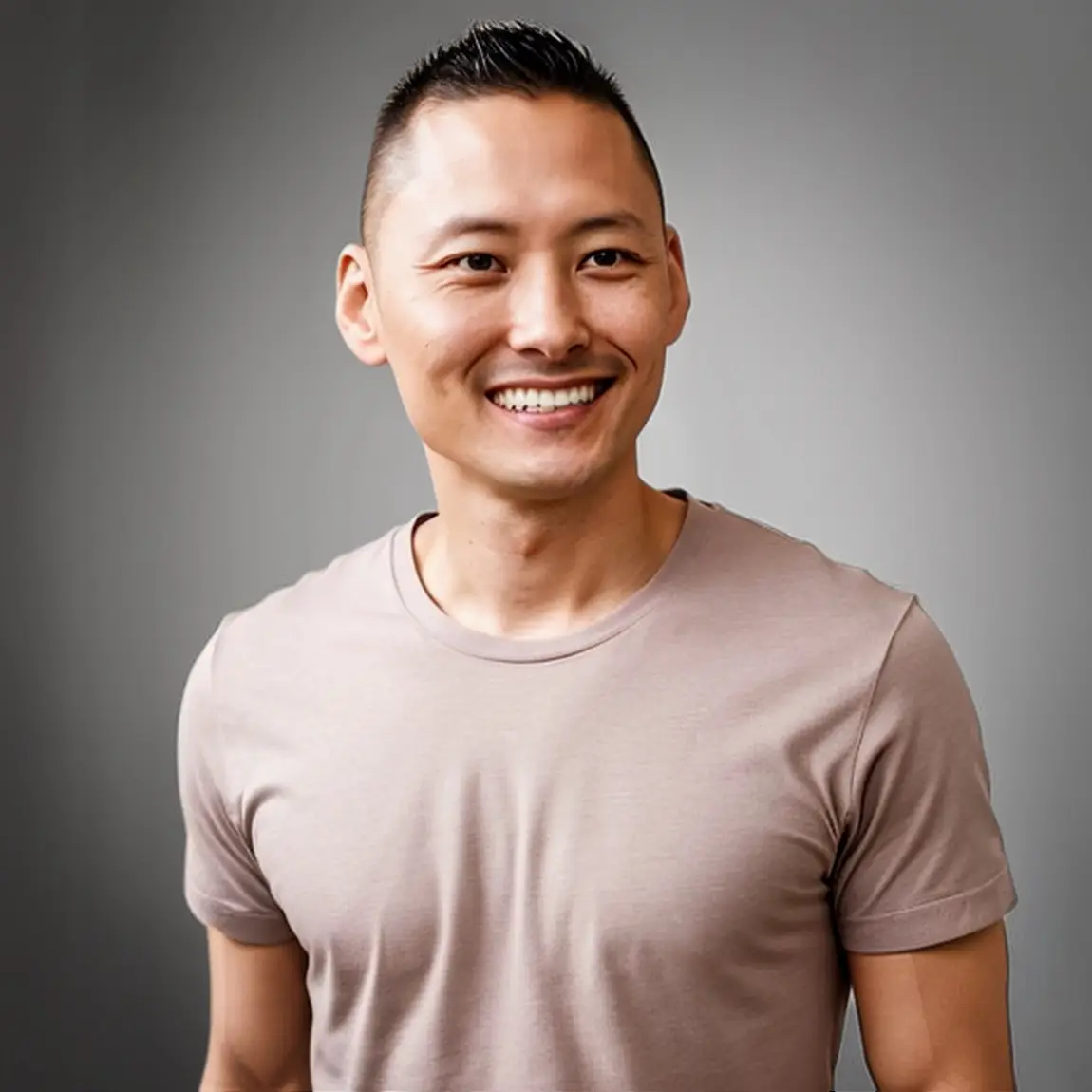 A smiling individual, Lewis Bertolucci, with a short hairstyle, wearing a light beige t-shirt, standing against a neutral gray background. The image exudes a friendly and approachable vibe, suitable for a personal website or professional profile.